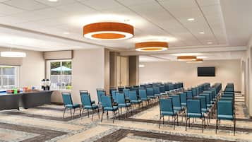 A conference room with rows of blue chairs, a stage, and a buffet area.