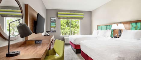 A hotel room with a desk, two beds, a chair, a TV, and large windows.