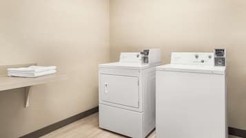 Une buanderie équipée de deux machines à laver et deux sèche-linge superposés, une étagère avec des serviettes pliées et un plancher en bois.