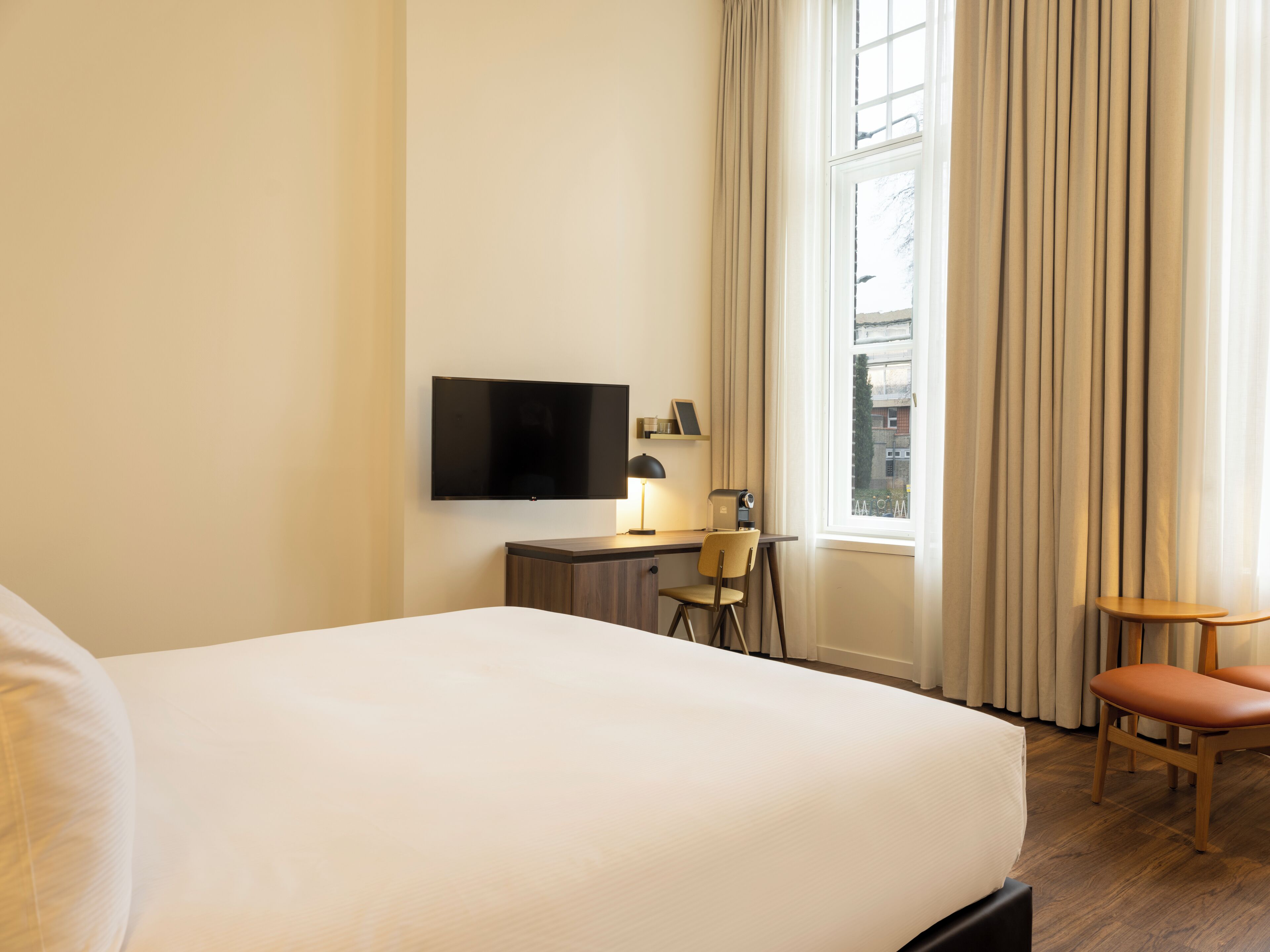A hotel room with a large bed, a desk with a chair, a television, and a window with curtains.