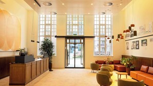 Un vestíbulo de hotel con mostrador de recepción, zona de estar, ventanas amplias y obras de arte en las paredes.