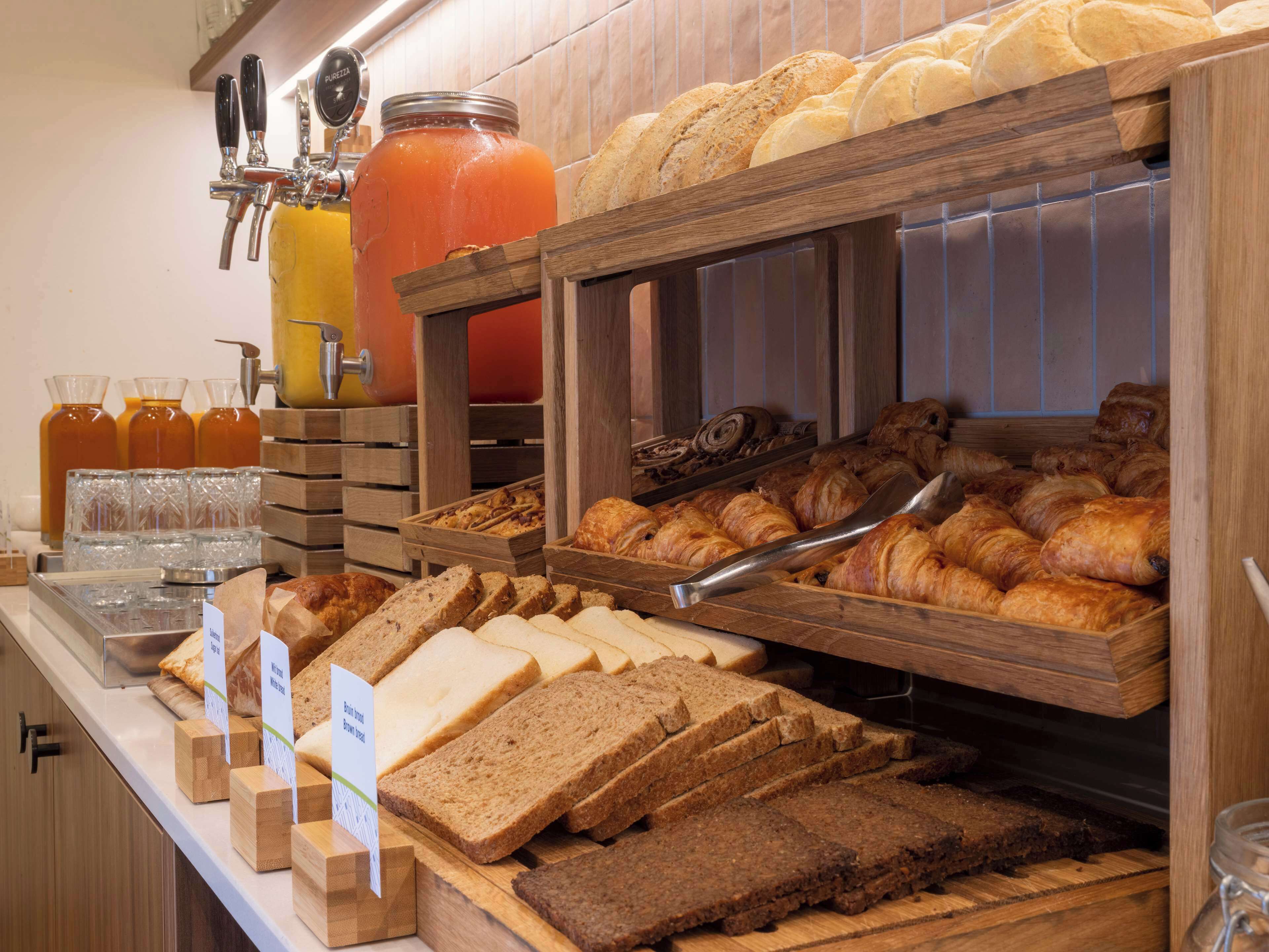 A breakfast buffet with various breads, pastries, and juices.