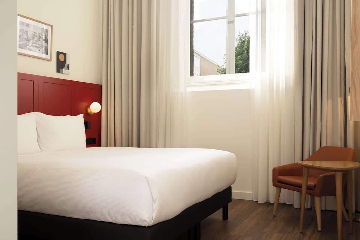 A hotel room with a bed, a chair, and a small table.