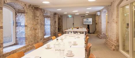 Un salón de conferencias con una larga mesa lista para una reunión, paredes de ladrillo y el logotipo de Hilton en la pared.
