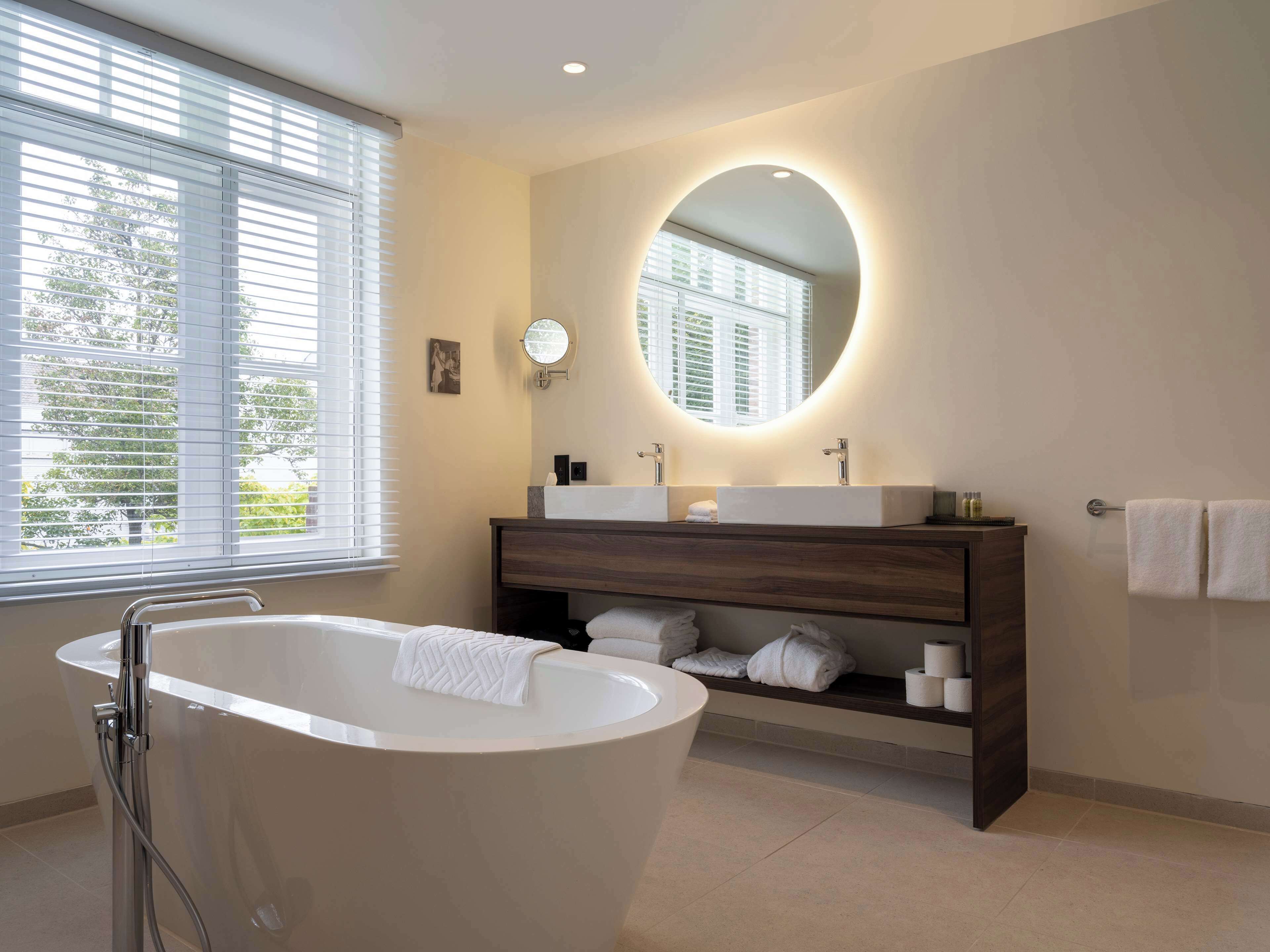 A modern bathroom with a freestanding bathtub, a vanity with a mirror, and a window with blinds.