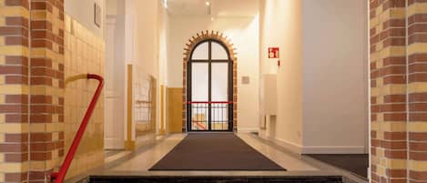 Un pasillo de hotel con pared de azulejos, barandilla roja y escalera empapelada de color negro que lleva a una puerta con panel de vidrio.