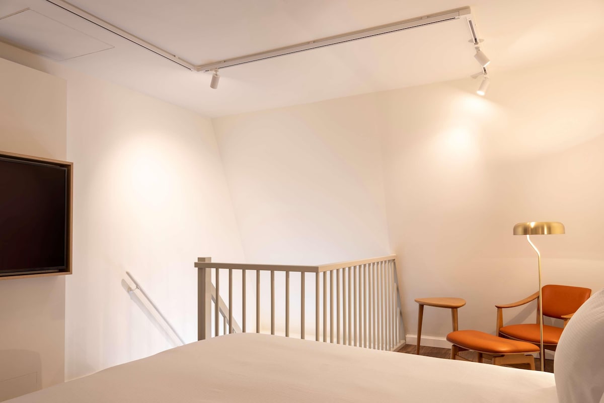 A hotel room with a bed, a desk, a chair, a TV, and a lamp.