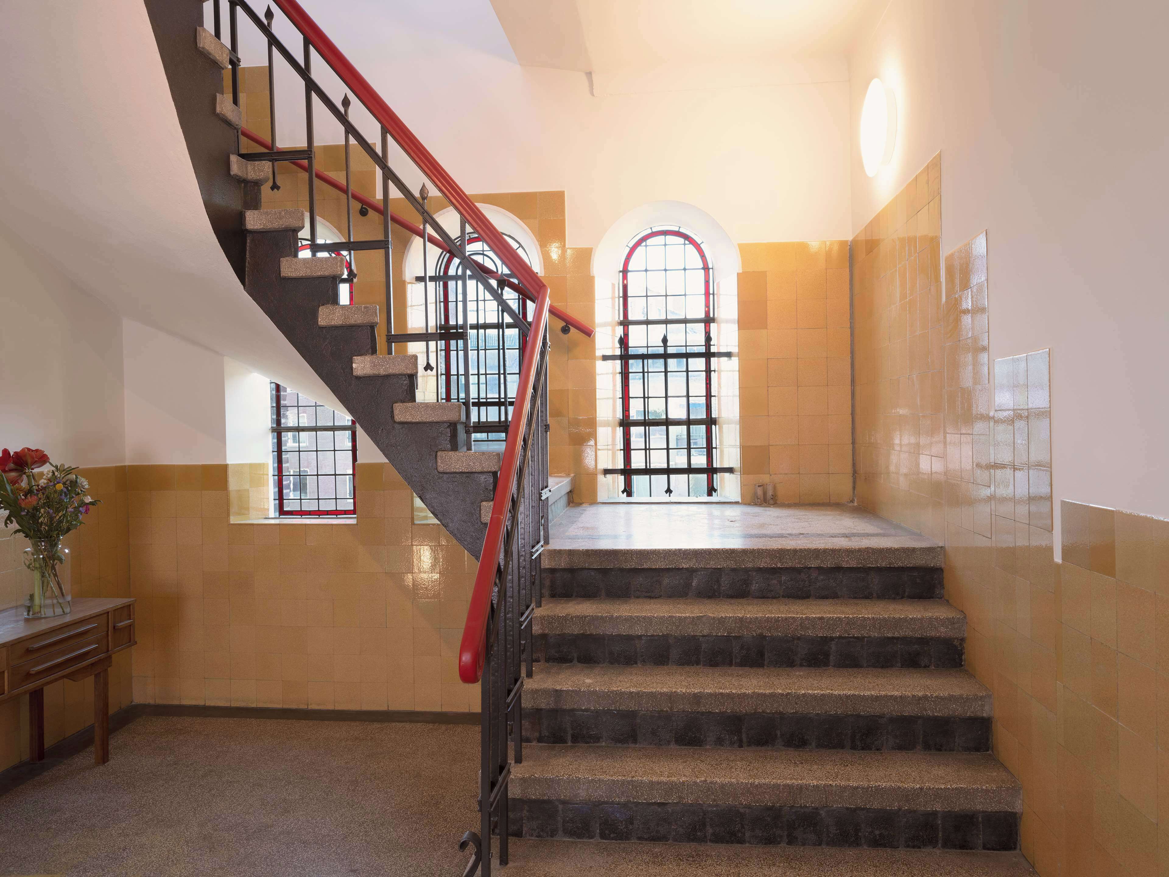 A staircase with a red handrail leading to a landing with a large arched window.