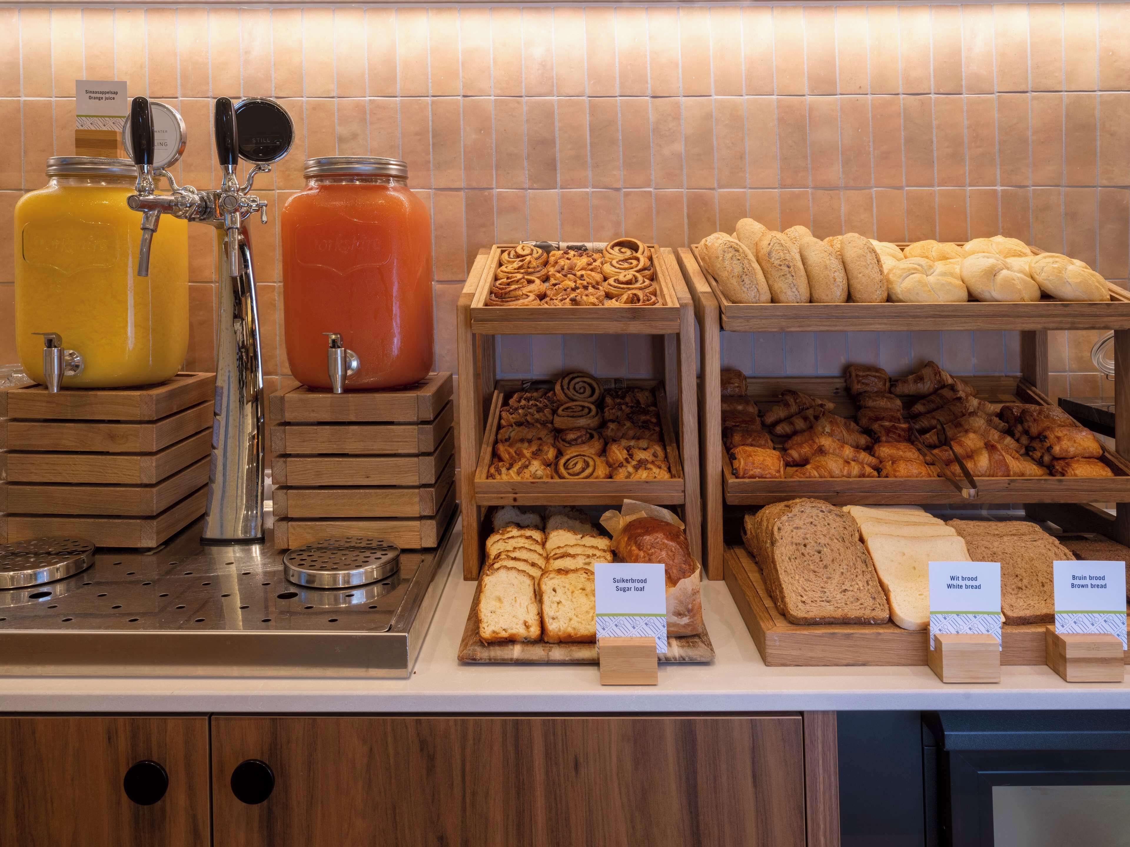 A breakfast buffet with various breads, pastries, and orange juice.