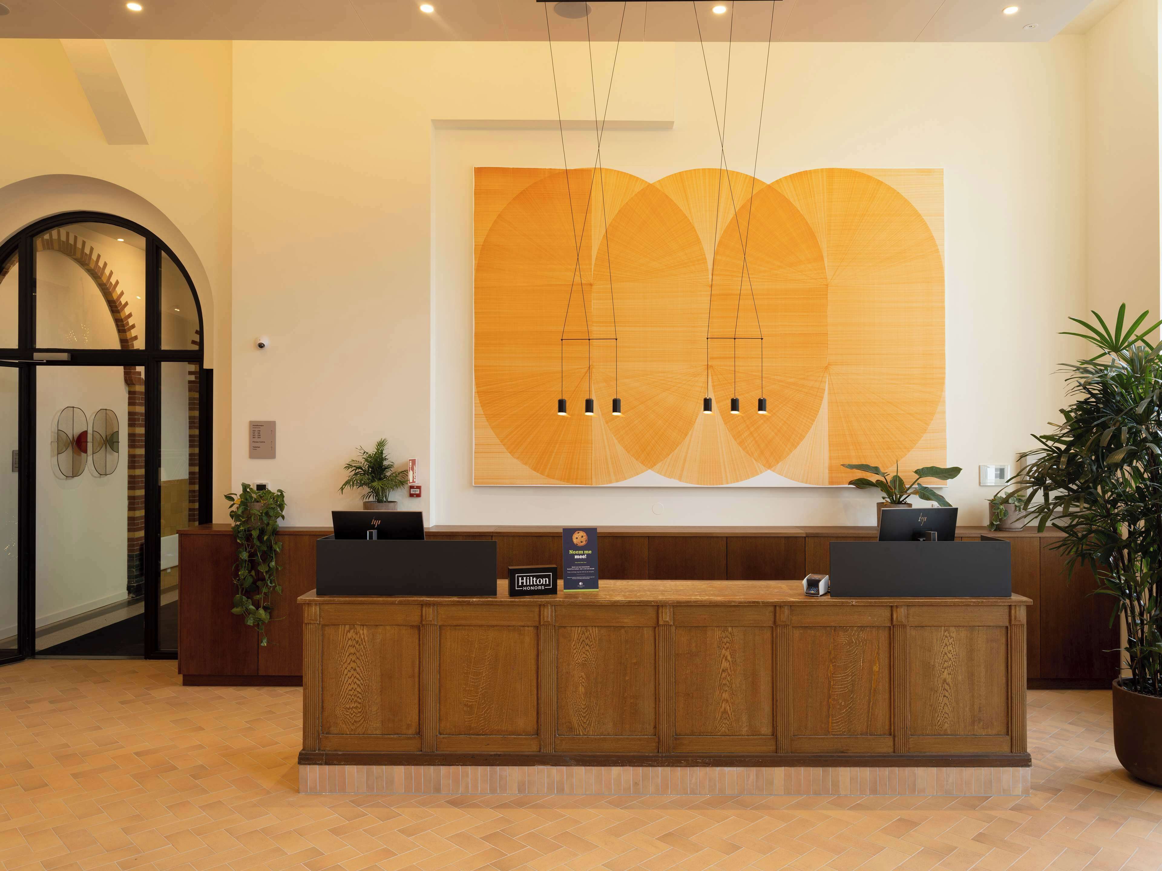 Una recepción con encimera de madera, dos monitores de ordenador y una gran obra de arte abstracta en la pared.