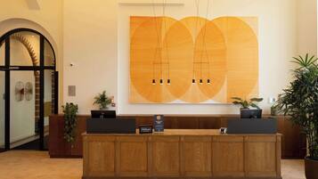 Una recepción con encimera de madera, dos monitores de ordenador y una gran obra de arte abstracta en la pared.