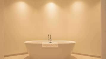 Une salle de bain moderne avec une baignoire sur pieds, des spots encastrés au plafond et un mur uni.