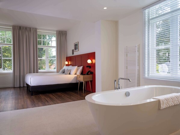 Un dormitorio moderno con una cama grande, una mesita de noche, un cabecero rojo, una lámpara de pared y un ventanal con cortinas.