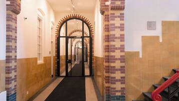 Un pasillo de hotel con alfombra negra, paredes de ladrillo y azulejos beige, y una escalera roja.