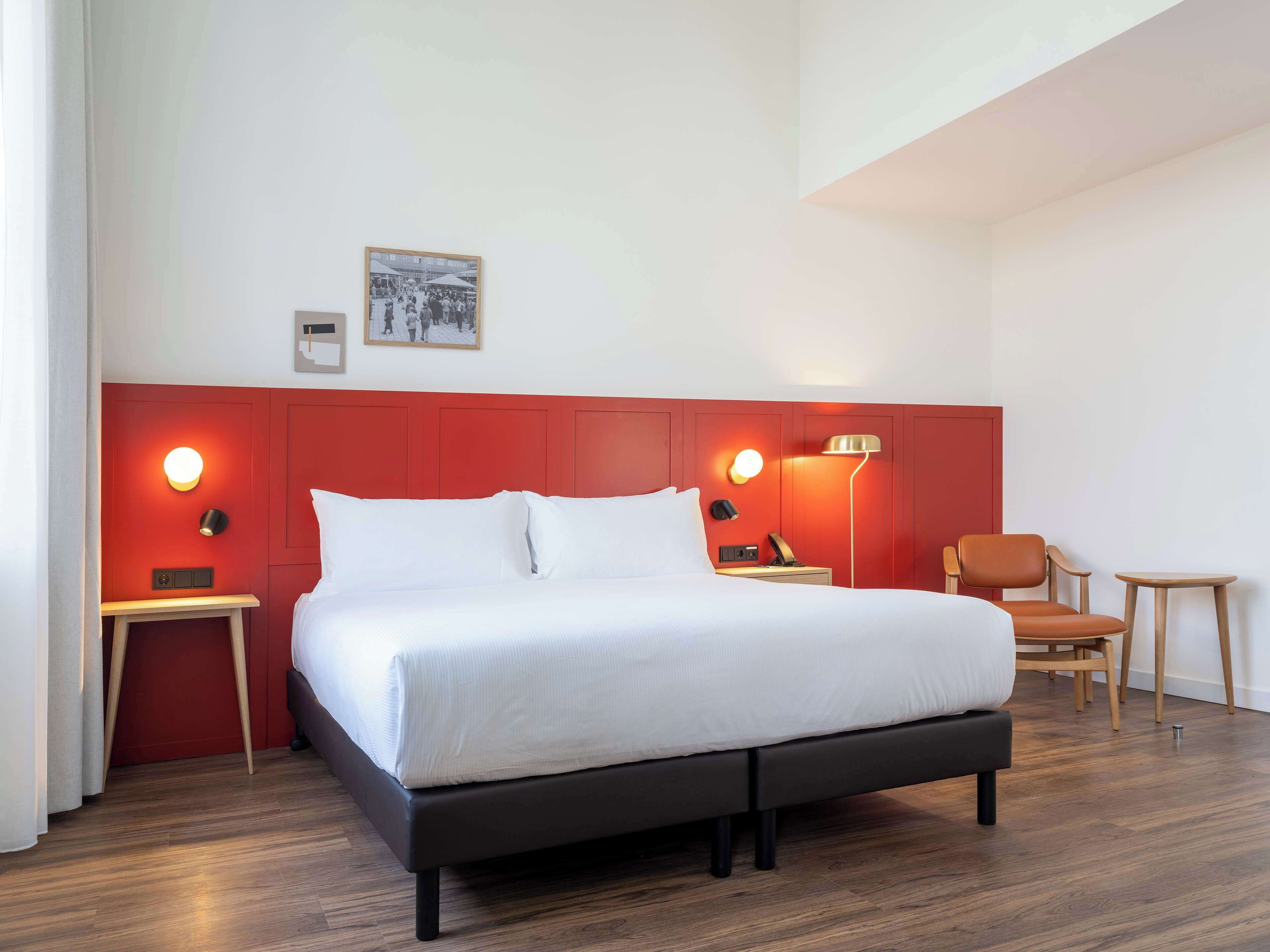 Une chambre d’hôtel moderne avec un grand lit, des murs d’un rouge vif et un petit coin salon.