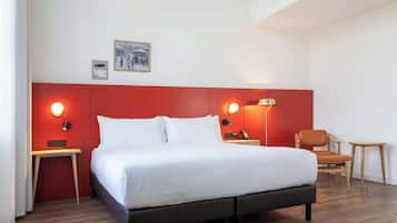 Een moderne hotelkamer met een groot bed, rode accentmuren en een klein zithoekje.