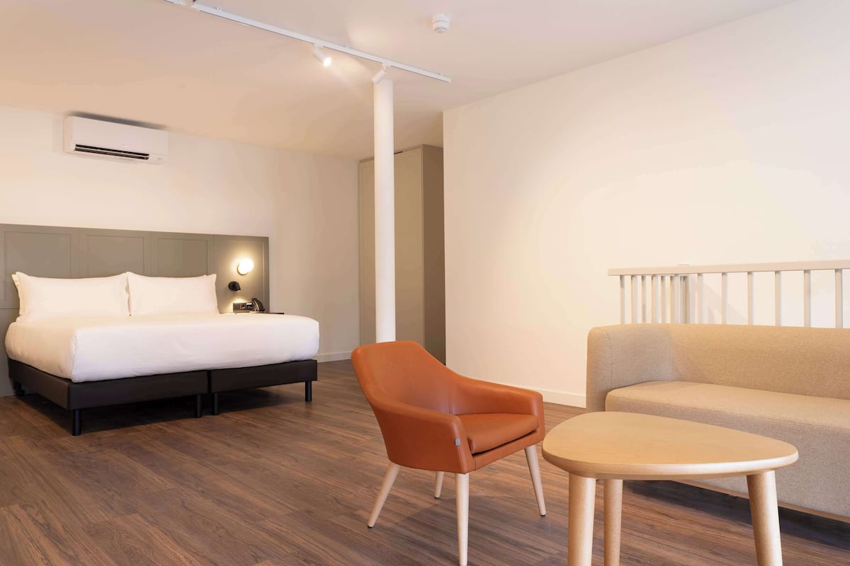 A modern hotel room with a bed, a chair, a sofa, and a small table.