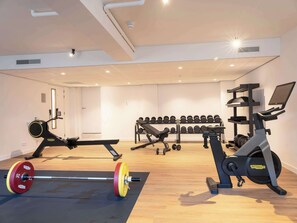 Un gimnasio con un banco de pesas, una cinta de correr y una estantería con mancuernas.
