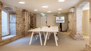 A conference room with a long table, white chairs, and a Hilton logo on the wall.