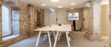 Un salón de conferencias con una larga mesa, sillas blancas y el logotipo de Hilton en la pared.