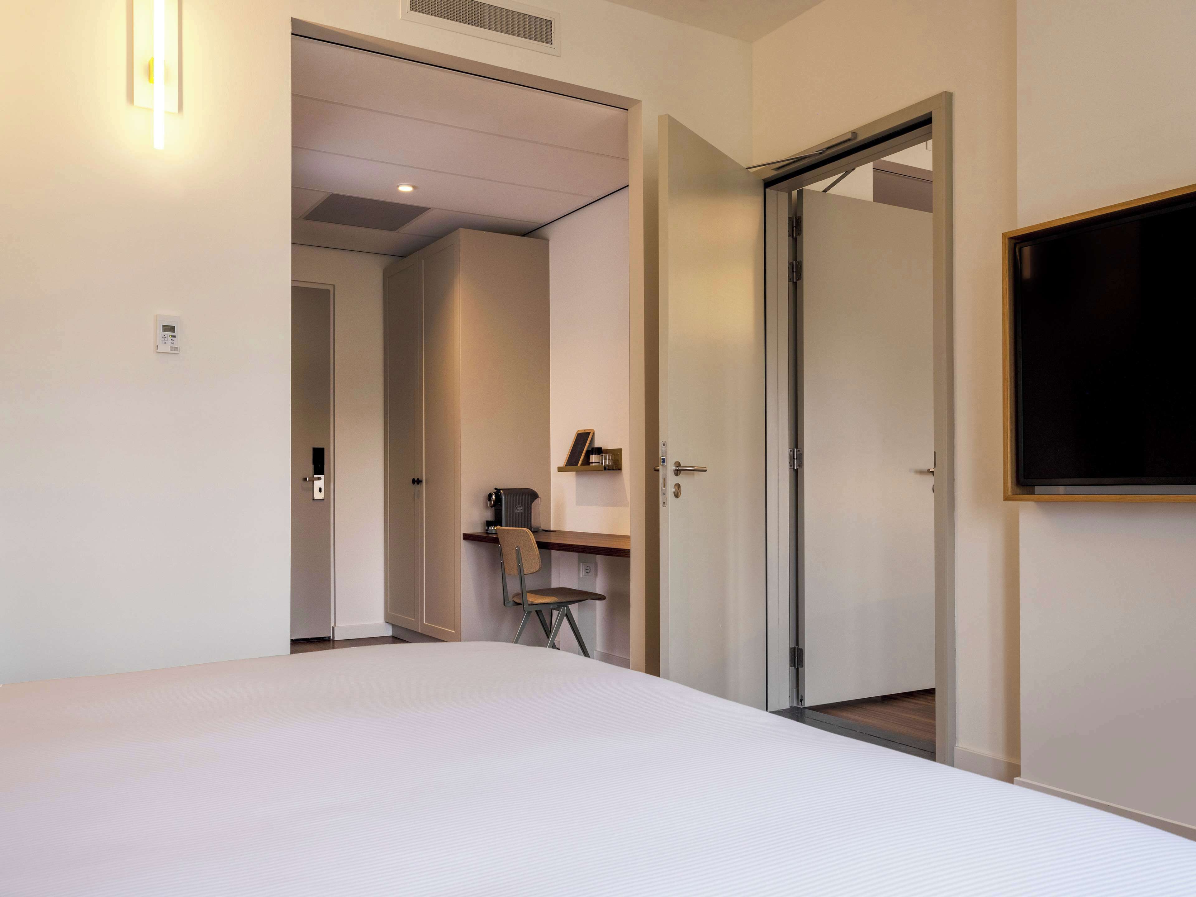 Habitació d'hotel amb un llit, una taula de treball, una cadira i una televisió.