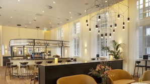 Zona de bar con taburetes, mostrador y lámpara colgante. Hay áreas de estar con sofás y una mesa.