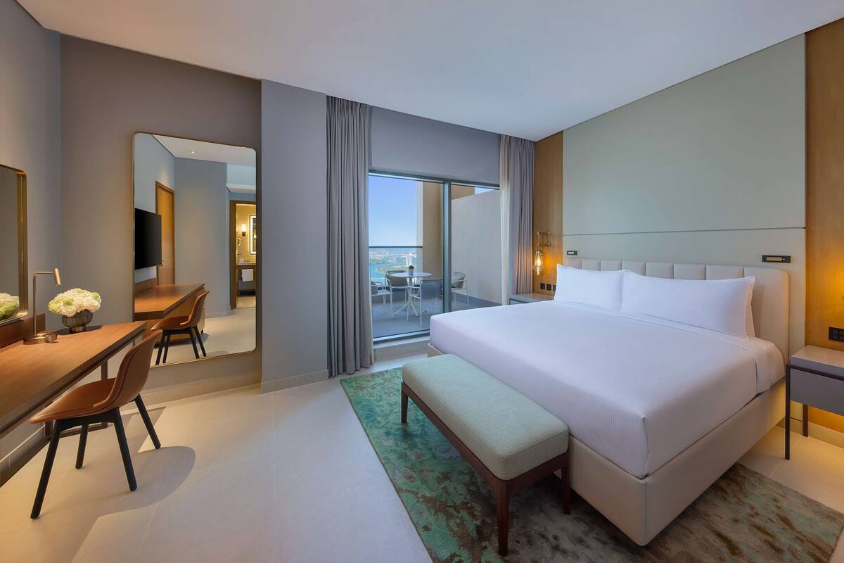 Een moderne hotelkamer met een groot bed, een bureau met stoel, een bankje en een grote spiegel.
