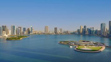 Un horizonte urbano frente al agua con edificios modernos altos, un puerto deportivo y una isla circular distintiva con un edificio en el centro.
