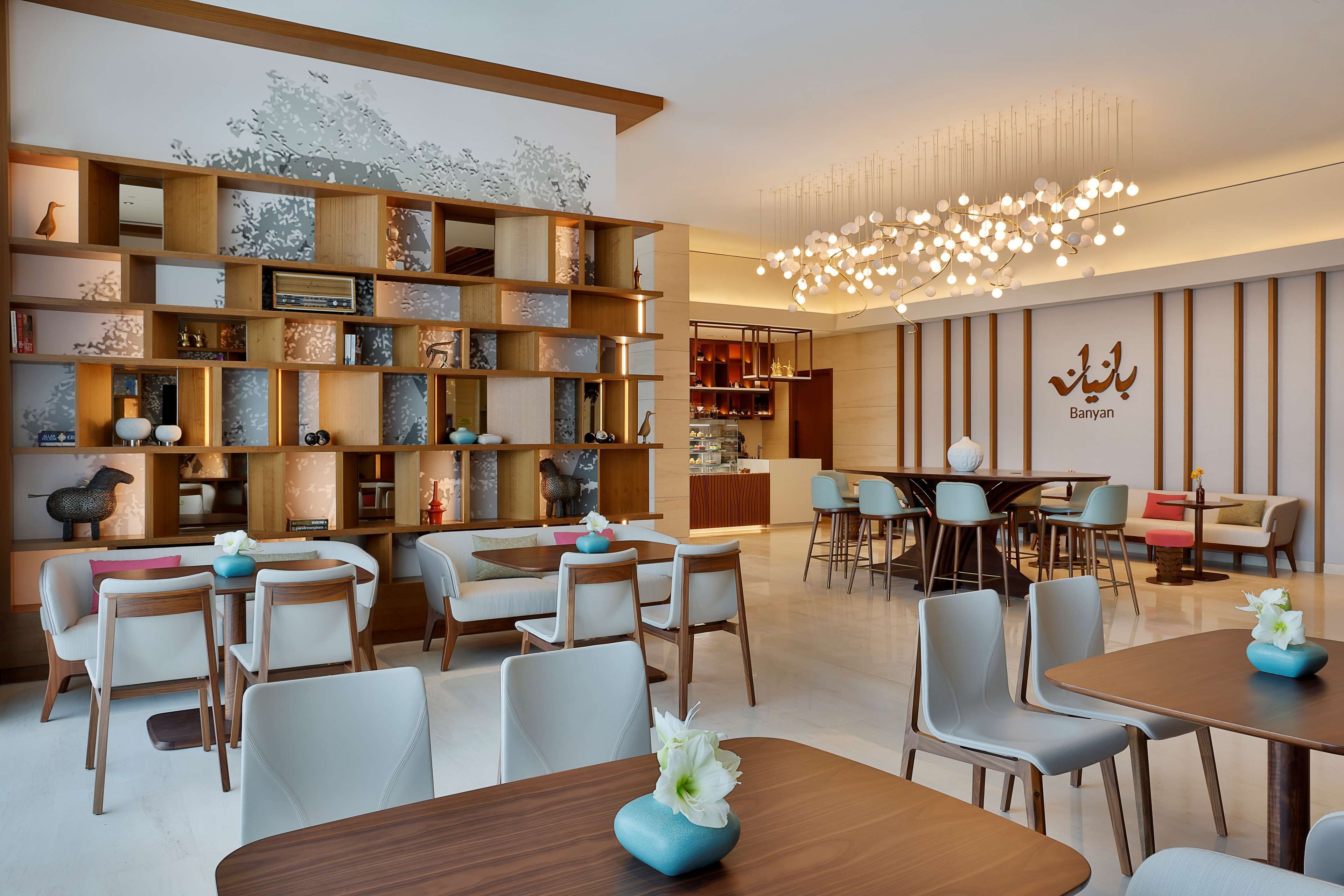 Una hall moderna di un hotel con una reception in legno, zone relax e una parete decorativa con mensole.