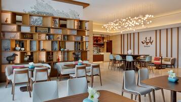 Una hall moderna di un hotel con una reception in legno, zone relax e una parete decorativa con mensole.