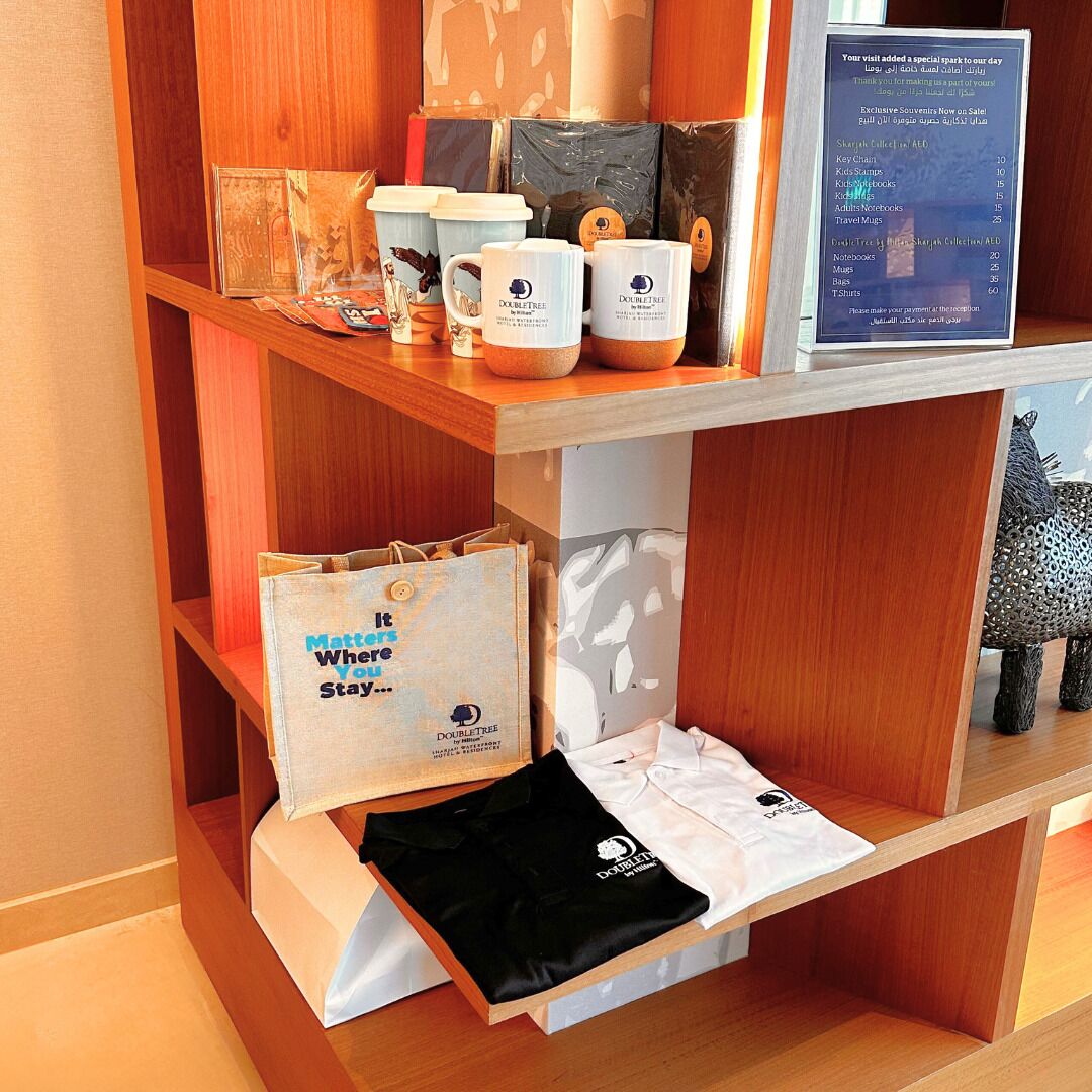 A display of DoubleTree-branded items including mugs, notebooks, and bags, with a wooden shelf and a signboard.