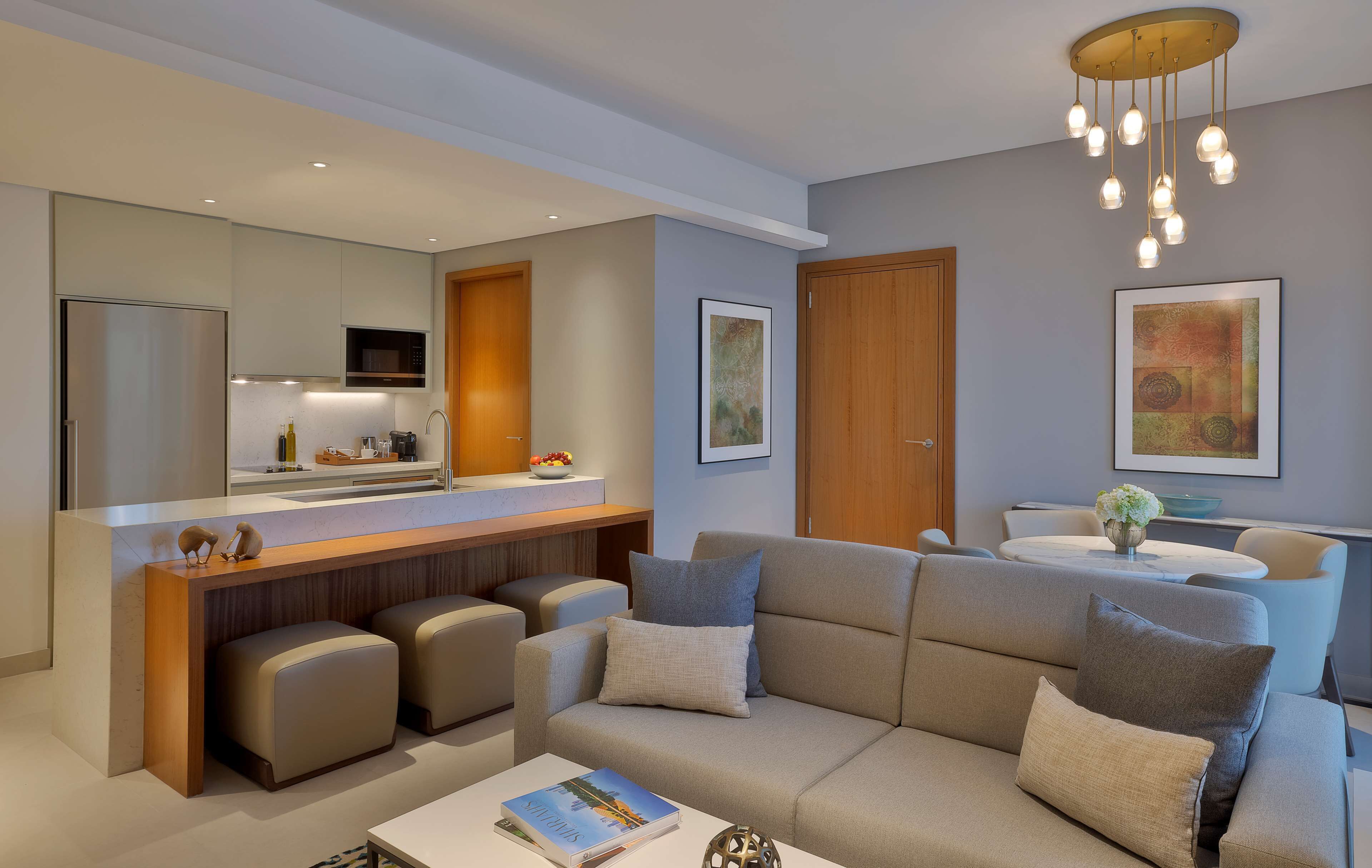 Una sala de estar moderna con sofá, otomanes, una mesa de centro y una cocina con refrigerador, microondas y mostrador.