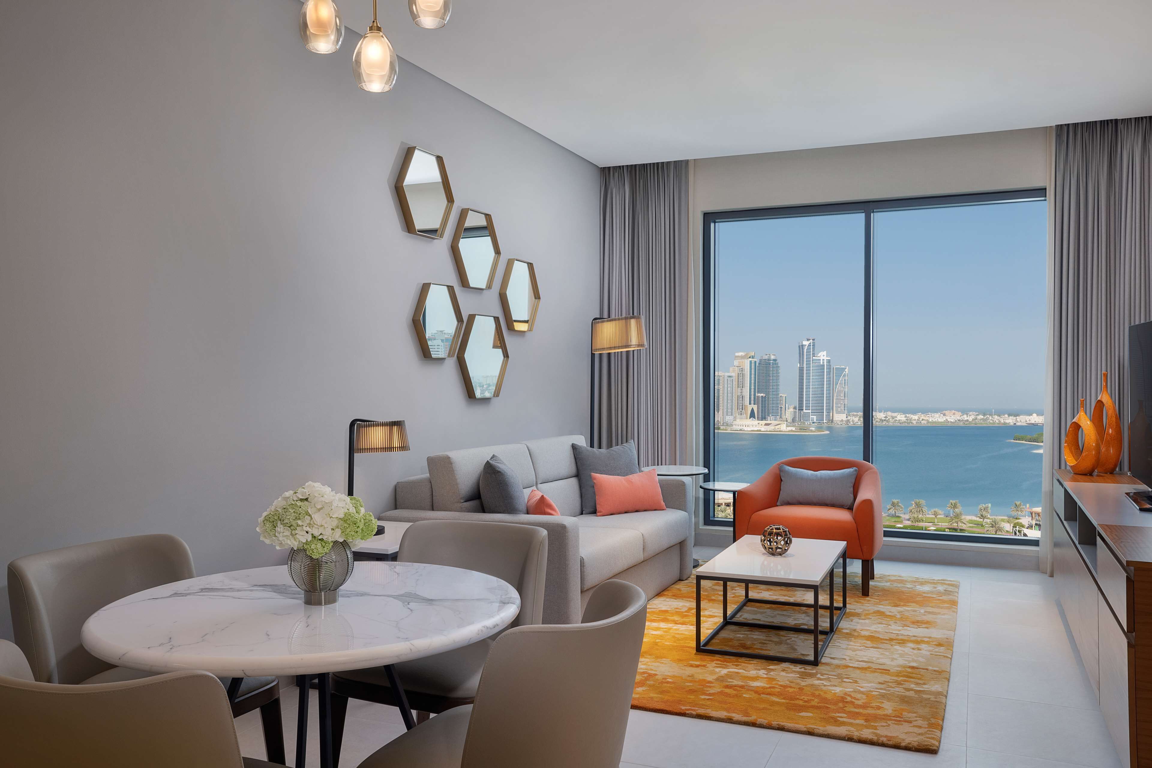 A modern living room with a large window, a sofa, a coffee table, and a dining area.
