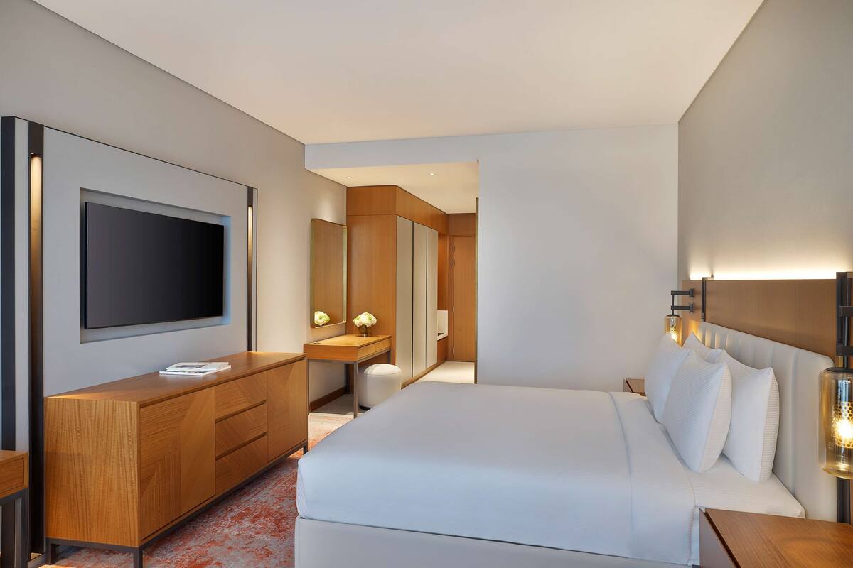 Een moderne hotelkamer met een groot bed, een houten dressoir, een flatscreen televisie, een kaptafel met spiegel en een nachtkastje met lamp.