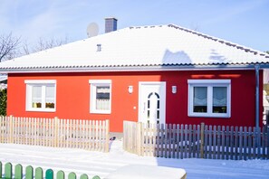 Et rødt hus med et hvidt stakhegn, en hvid dør og en parabol på taget.