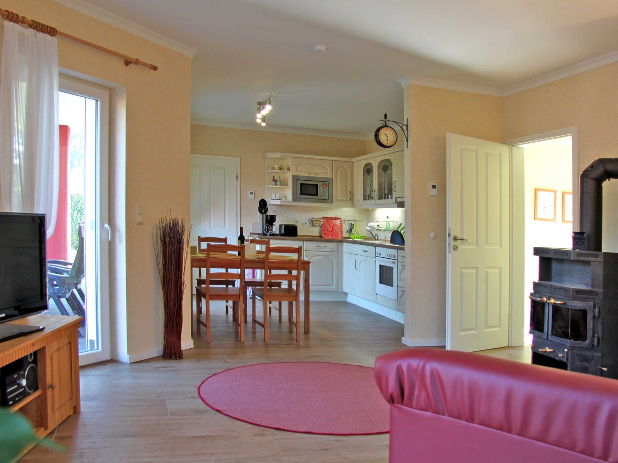 Una sala de estar con televisor, un sofá rojo y una cocina al fondo.
