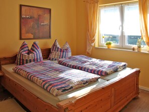 A double bed with striped bedding, a wooden headboard, a window with curtains, and a small plant on the windowsill.