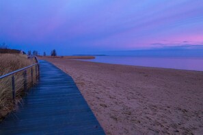 A wooden boardwalk leading to a sandy beach with a calm body of water.