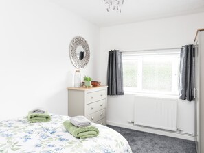 Une chambre à coucher comprenant un lit, une commode, un miroir, une fenêtre avec des rideaux et un radiateur.
