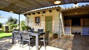 An outdoor patio with a table and chairs, a covered area with a thatched roof, and a brick oven. - 44262 Finca Els Xiprers (Porreres)