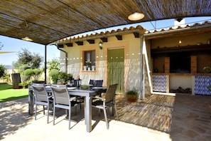Une terrasse extérieure avec une table et des chaises, un espace couvert avec un toit de chaume et un four en briques.
