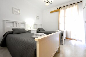 Un dormitorio con dos camas, una mesita de noche, una lámpara y una ventana con cortinas.