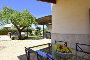 Un patio al aire libre con mesa y sillas, un frutero y una zona de estar cubierta bajo una pérgola.
