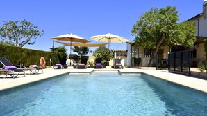 Une piscine entourée d’une haie et d’arbres, avec des chaises longues et des parasols.