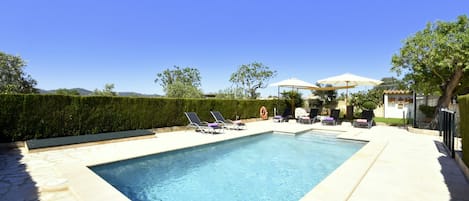 A rectangular swimming pool with a stone border, surrounded by lounge chairs and umbrellas.