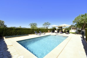 Une piscine rectangulaire bordée de pierres, entourée de chaises longues et de parasols.