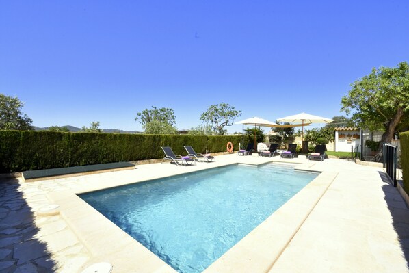 A rectangular swimming pool with a stone border, surrounded by lounge chairs and umbrellas.