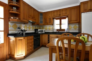 Una cocina con armarios de madera, encimera negra, microondas y una mesa de comedor con sillas.