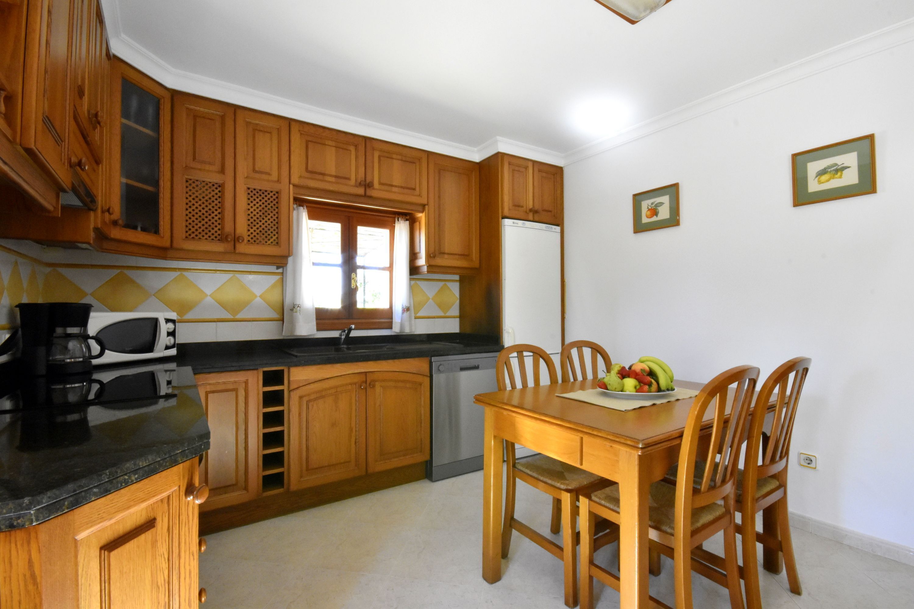 A kitchen with wooden cabinets, a black countertop, a stainless steel dishwasher, and a dining table with chairs.