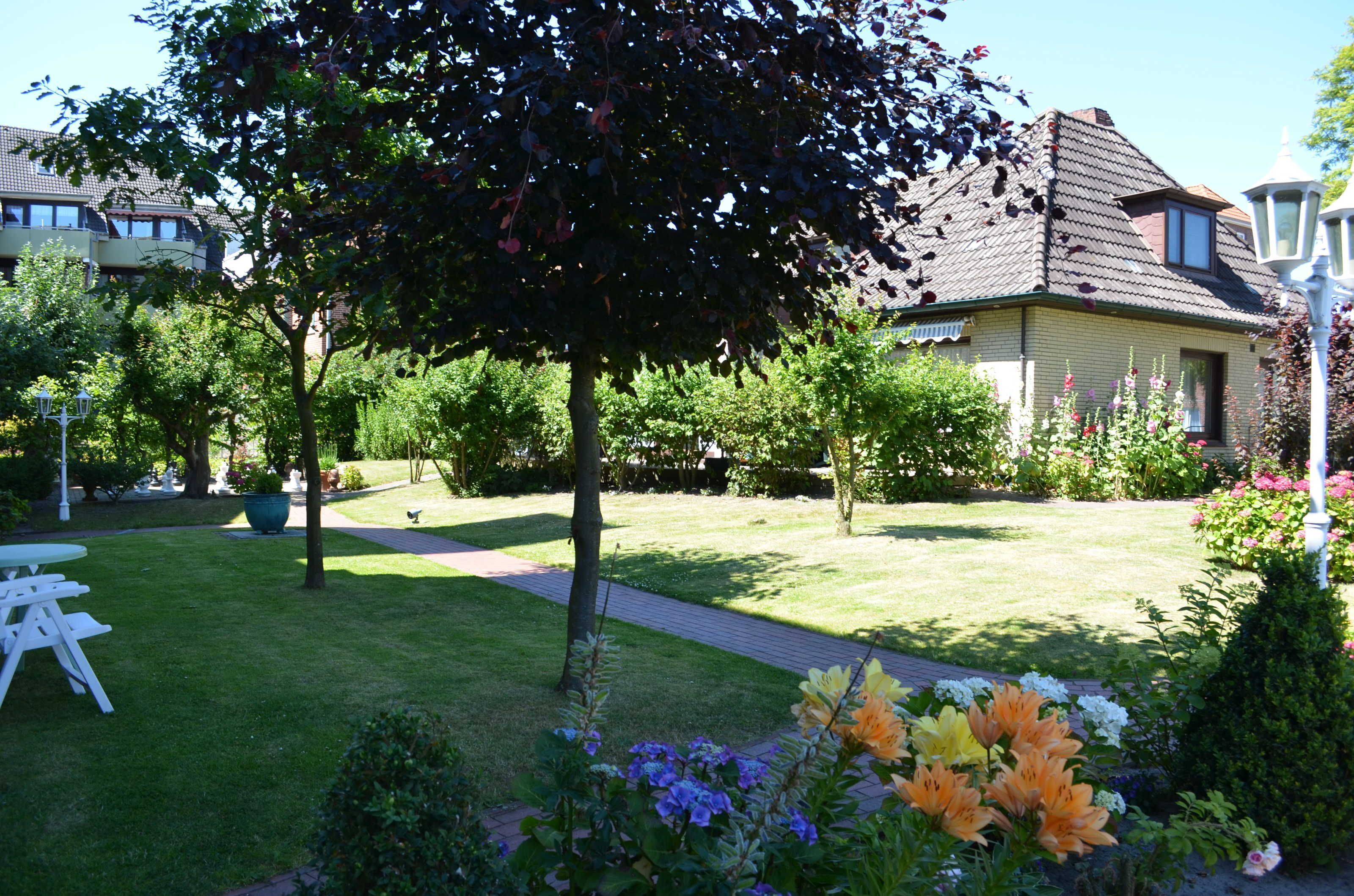 Een tuin met gras, een pad en een witte tafel met stoelen.